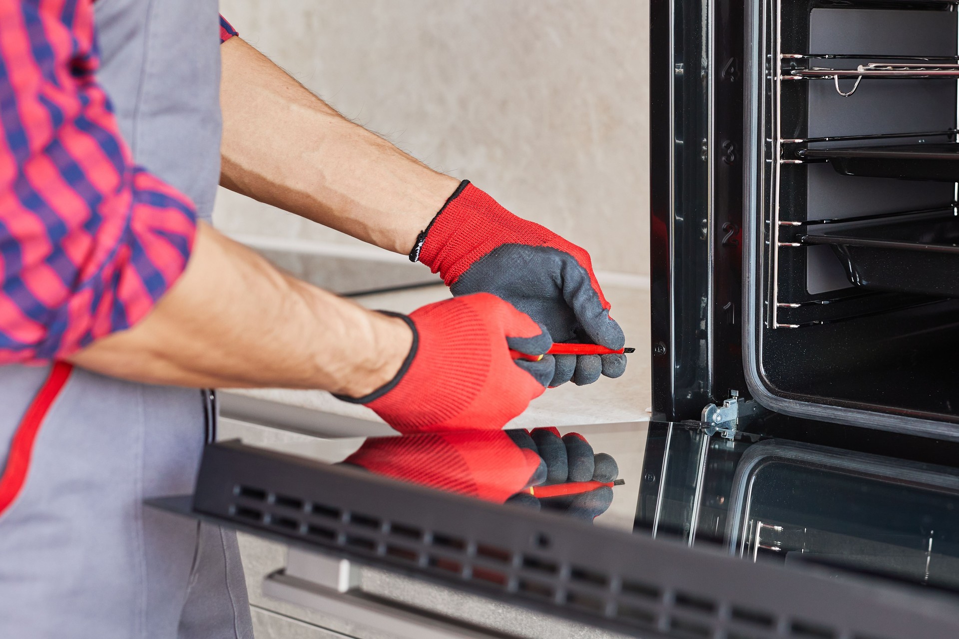 Worker repairs electric oven in kitchen. Repairman works with screwdriver install and checking oven at client home. Man assemblying appliances in kitchen furniture.